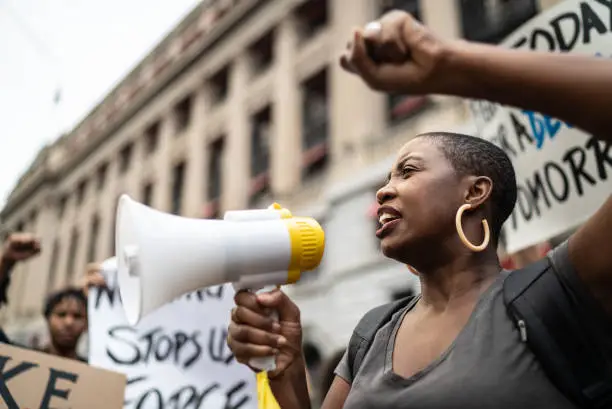 Femme tenant un mégaphone lors d'une manifestation, poing levé — prise de parole contre les injustices.